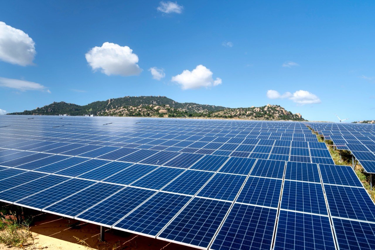 Champ de panneaux photovoltaïques sous un grand ciel bleu et nuageux